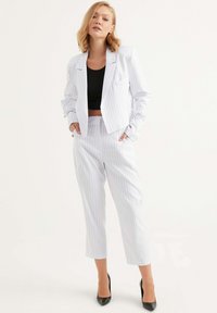 Vit blazers med ränder och matchande korta byxor, med en svart topp under. Materialet verkar slätt; blazern har en enkel ficka.