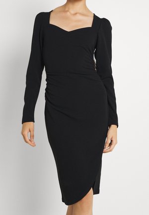 Vestido negro de manga larga con escote cuadrado, detalle fruncido en los costados y dobladillo estilo cruzado. Textura de tela suave, silueta ajustada.