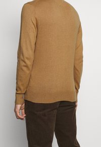 Brauner Wollpullover mit gerippten Bündchen und Saum, mit Rundhalsausschnitt und glatter Textur, kombiniert mit dunkelbraunen Cordhosen.