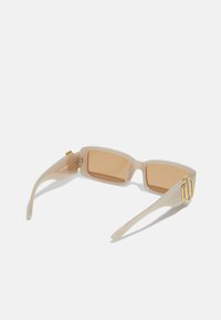Gafas de sol rectangulares beige con lentes tintados, armazón transparente y acento en metal tono dorado en la patilla. Textura suave en toda su superficie.