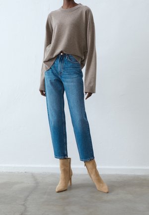 Béžový pletený svetr se širokými rukávy, kombinovaný s světlými modrými džíny s vysokým pasem a taupe kotníkovými botami se zipem.