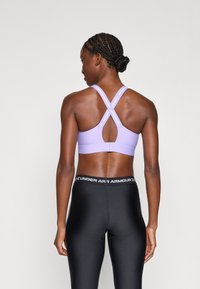 Violeta sporta krūšturis ar sacensību atpakaļu dizainu, kuram ir atslēgas caurums. Melni pieguļoši legingi ar "Under Armour" logotipu uz jostas.