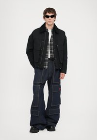 Musthave musta lühike jakk, millel on karvane krae, kihtidena seljas ruuduline särgid. Lõdvike denimist cargo püksid, millel on mitmed taskud ja punased aktsendid.