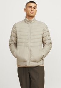 Beige pufferjakke med vandret quiltet design, høj krave, lynlåsforting og sidelommer. Let materiale, glat tekstur.