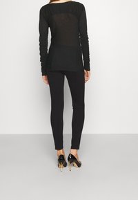 Zwarte top met lange mouwen en geplooide details aan de achterkant, gecombineerd met zwarte legging en zwarte pumps. Overal een gladde textuur.