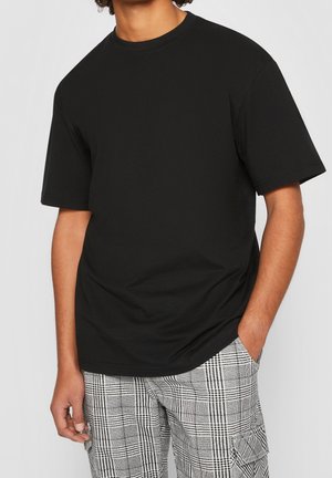 Camiseta negra de algodón con cuello redondo y mangas cortas, combinada con pantalones a cuadros gris y blanco con bolsillos.
