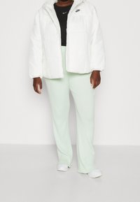 White puffer jacket with a hood and textured finish, worn over a black Nike top and mint green ribbed pants paired with white shoes.