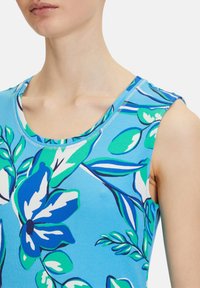 Ärmlös topp i ljusblått bomull med gröna och blå blommönster, med rundad halsringning och subtil ribbad struktur.