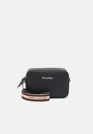 Czarna prostokątna torba na ramię z złotym zamkiem błyskawicznym, logo Tommy Hilfiger oraz odczepianym paskiem z taśmy z nazwą marki i paskowanym wzorem.