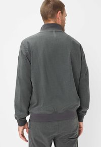 Mann in grauer lässiger Jacke und passender Hose, von hinten gezeigt, der Rücken und die Kragen Details werden vor einem schlichten weißen Hintergrund präsentiert.