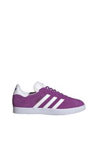 Baskets en suède violet avec des rayures et des accents blancs. Elles présentent une semelle en caoutchouc blanc texturé et un renfort au niveau du talon. Nom du modèle : Gazelle.