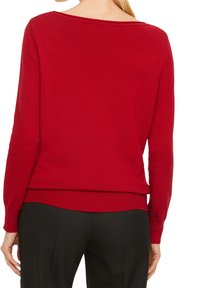Pull en maille rouge avec un col large et des poignets côtelés. Texture lisse avec une taille ajustée. Porté sur un pantalon noir.