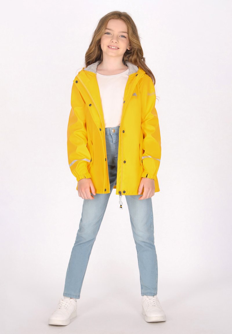 Geltonas nepralaidus vandeniui švarkas su pilku gaubtu, juodais mygtukais ir atspindinčiomis detalėmis, dėvimas virš balto marškinėlio ir šviesiai mėlynų džinsų.