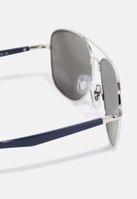 Occhiali da sole in metallo con lenti grigie, montatura argentata e stanghette blu navy. Presentano naselli regolabili e logo sulla stanghetta.