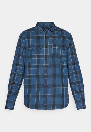 Camisa xadrez azul com mangas longas, botão na frente, dois bolsos no peito e uma textura suave. Apresenta linhas em grade brancas e cinzas.