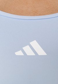 Ljusblå träningsöverdel med ribbstruktur, med en framträdande vit logotyp i geometrisk design på framsidan.