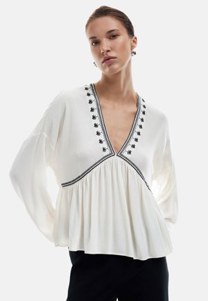 Weiße Bluse mit langen Ärmeln und tiefer V-Ausschnitt, mit schwarzem floralen Stickerei und einem gerafften Design an der Taille, aus strukturierter Stoff gefertigt.