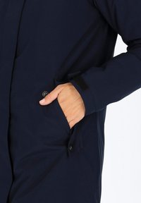 Granatowa kurtka z boczną kieszenią, zapięciem na guziki, akcentem z rzepem przy mankietach oraz gładką, trwałą teksturą materiału.