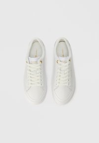 Een paar witte leren sneakers van Tommy Hilfiger met veters, gouden oogjes en gouden branding op de tong en zijkant, van bovenaf gezien.