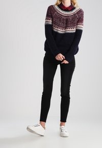 Dunkelblauer Pullover mit einem rot-weißen gemusterten Einsatz, kombiniert mit schwarzen Skinny Jeans und weißen Sneakers. Der Pullover hat ein strukturiertes Strickmuster.