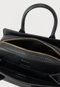 Crna kožna torba s teksturiranom vanjštinom, zlatnim patentnim zatvaračem i dva ručka. Unutrašnjost ima prostrani pretinac s detaljima džepa.