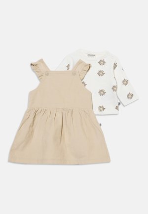 Robe bébé beige sans manches avec bretelles à volants, associée à une chemise blanche à manches longues avec imprimés de fleurs marron.