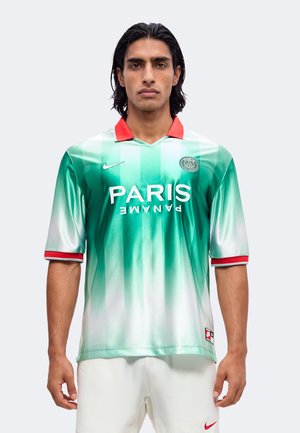 Homme aux cheveux noirs mi-longs portant un maillot de football vert et blanc du Paris Saint-Germain avec un col rouge et un short blanc.