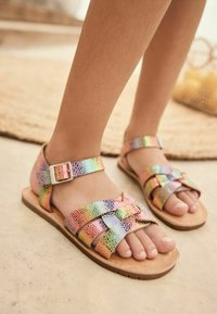 Colorful, iridescent sandals with crisscross straps and a buckle, featuring a natural leather footbed and a flat sole.