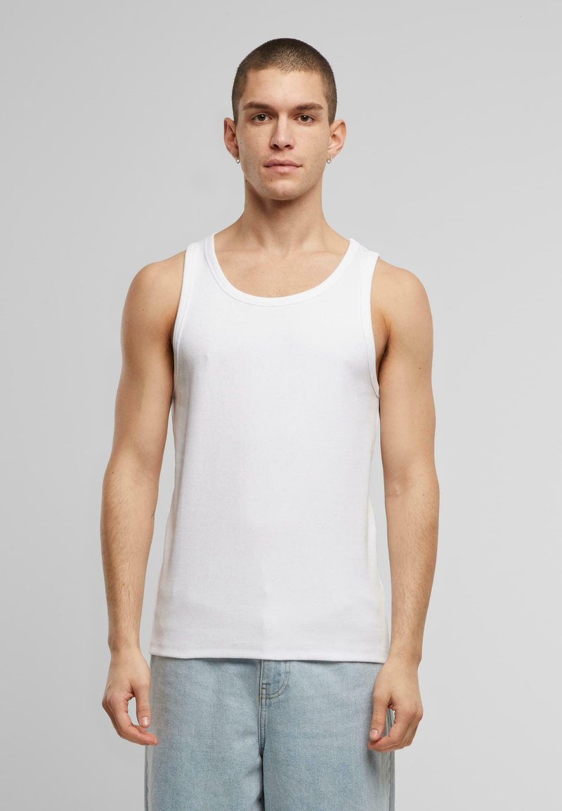 Hvid bomulds tanktop, ribbet tekstur, rund udskæring, tætsiddende design, båret med lyseblå denim shorts, model vendt mod kameraet mod en ensfarvet baggrund.
