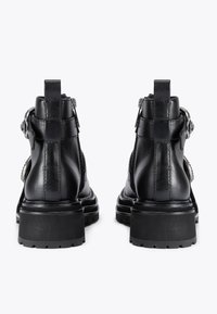 Czarne skórzane botki za kostkę z dużymi obcasami, srebrnymi akcentami oraz teksturowanym wykończeniem. Posiadają solidną podeszwę i detal w postaci klamry po boku.