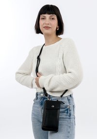 Black leather crossbody bag with a smooth texture, a front flap, a snap closure, and adjustable strap, worn with a cream knit sweater.