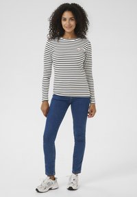 Langarmshirt met strepen in wit en zwart, gemaakt van zacht katoen, voorzien van een klein hartlogo. Gecombineerd met een blauwe spijkerbroek en witte sneakers.