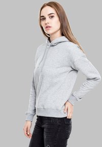Un sweat à capuche gris avec un cordon de serrage, des poignets et un ourlet côtelés. Tissu doux, coupe décontractée, poches latérales, porté avec un jean noir. Design sobre.