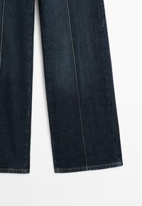Dunkelblaue Schlagjeans mit kontrastierenden Nähten, einer glatten Denim-Oberfläche und geradem Schnitt. Hat keine sichtbaren Verzierungen.