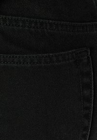 Svart denimtyg med en slät yta, som har en framficka och kontrasterande sömmar längs kanterna. Enkelt och funktionellt design.