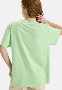 Mintgrünes, übergroßes T-Shirt aus weicher Baumwolle. Kurze Ärmel, Rundhalsausschnitt und ein dezentes Logo-Detail hinten am Halsbereich.