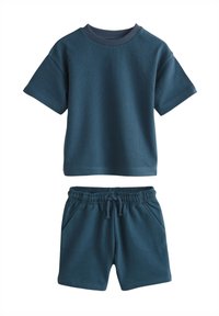 Krátké rukávy tmavě petrolejového pleteného trička a odpovídající kraťasy s elastickým pasem položeny na rovné ploše, neformální letní outfit.