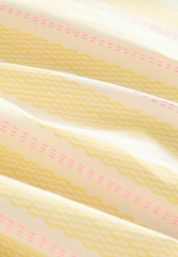 Lätt tyg med en mjuk textur som har ett upprepande mönster av gula och rosa geometriska former på en blek bakgrund.