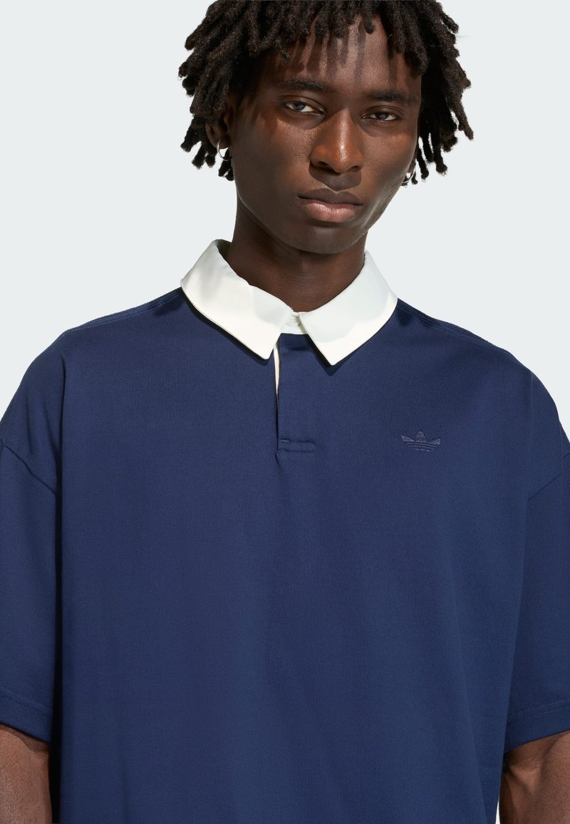 Navy blue polo shirt with a white, pointed collar, featuring a small embroidered logo. Made from soft fabric with a relaxed fit and short sleeves.