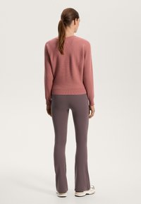 Pink ribbed sweater with long sleeves paired with fitted grey flared pants. The outfit features a relaxed fit and subtle texture details.