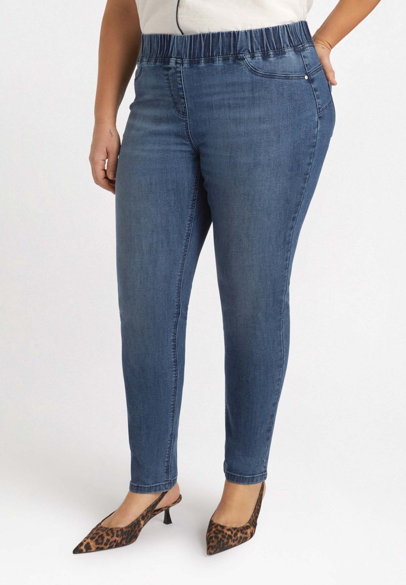 Femme portant un jean skinny taille élastique bleu associé à des escarpins slingback à talons kitten pointus imprimé léopard.