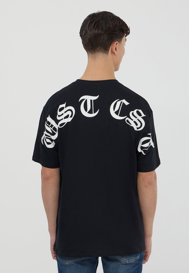 T-shirt in cotone nero con grande testo bianco stilizzato sulla schiena e sulle maniche. Design a girocollo con maniche corte, vestibilità rilassata.