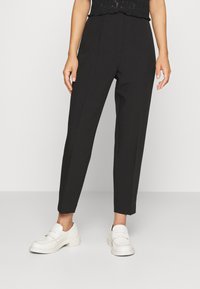 Black tailored trousers with a high waist, straight leg fit, and front crease, paired with white loafers featuring prominent stitching details.