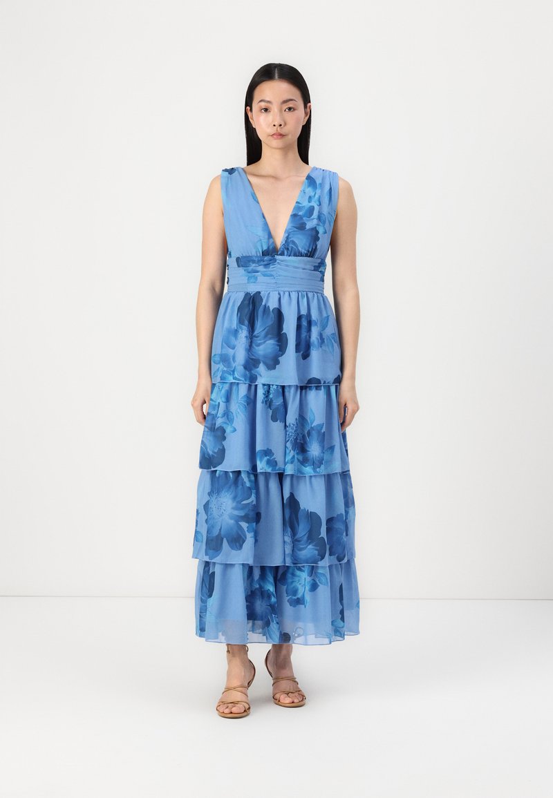 Zila ziedu maksi kleita ar dziļu V veida kaklu, kārtotiem volāniem un pieguļošu vidukli. Audums izskatās viegls un plūstošs.