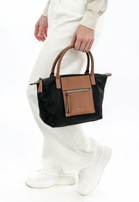 Borsa nera e marrone realizzata in materiale testurizzato, con una tasca frontale con zip, manici corti e dettagli in crema. Design compatto e strutturato.
