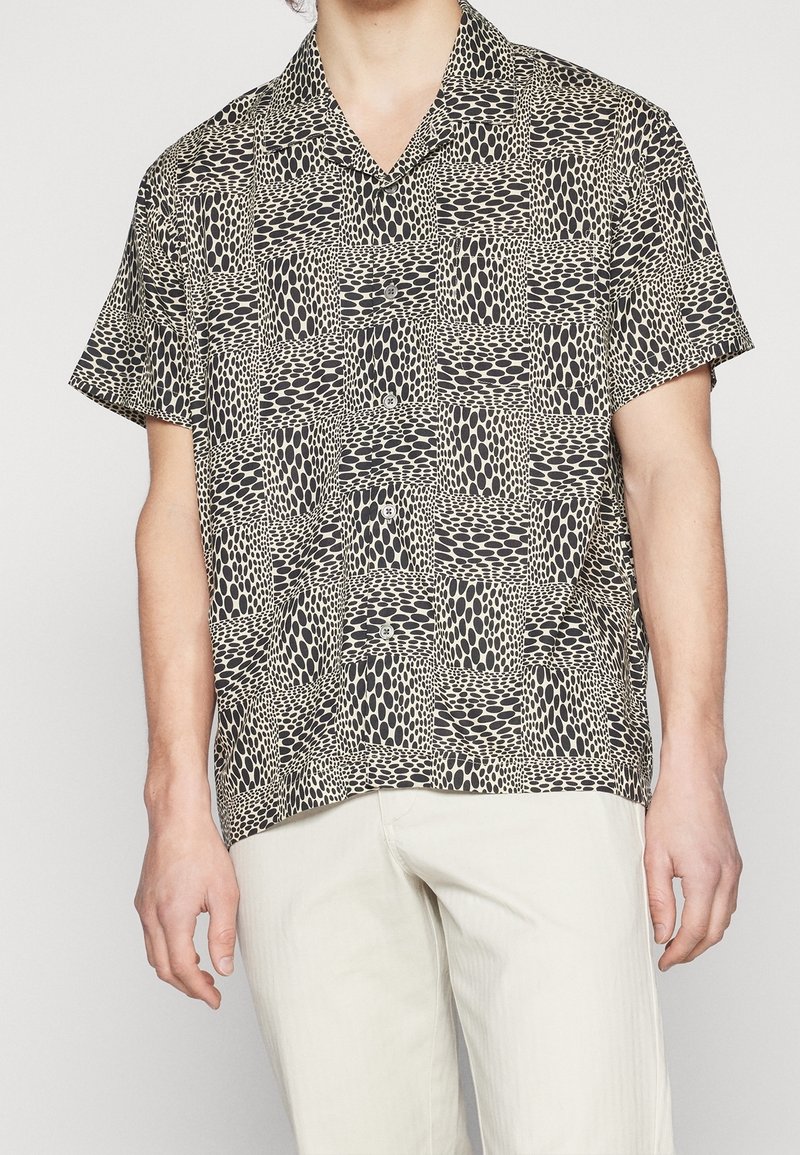 Košile s krátkým rukávem v světle béžové a černé barvě se vzorem obdélníkových a oválných tvarů, se rozšířeným límcem a zapínáním na knoflíky.