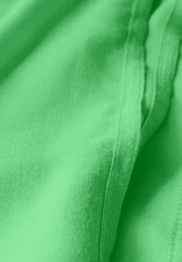 Tissu vert vif avec une surface lisse et texturée. Présente des coutures et des plis visibles, montrant la fluidité de la drapé et la douceur du matériau.