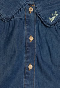 Denim shirt in dark blue with a frilled collar, featuring five wooden buttons down the front and contrasting stitching. "Levi's" logo in green embroidery.