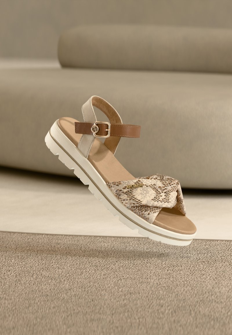 Sandales beiges avec une bride avant imprimé serpent, une bride de cheville en cuir et une semelle en caoutchouc blanche. Elles comportent une boucle décorative et une surface texturée.