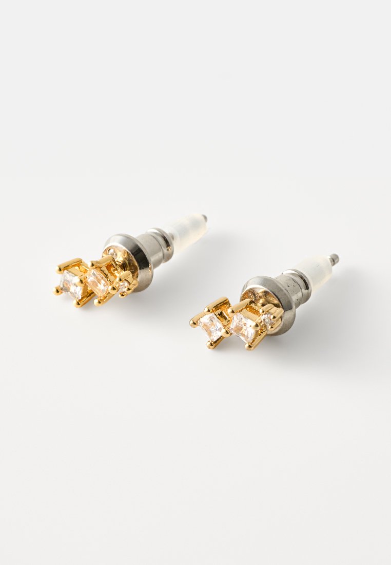 Goldfarbene Steckerohrringe mit zwei klaren quadratischen Edelsteinen in einer Krappenfassung, Metallrücken und transparentem Stift für einen sicheren Sitz.
